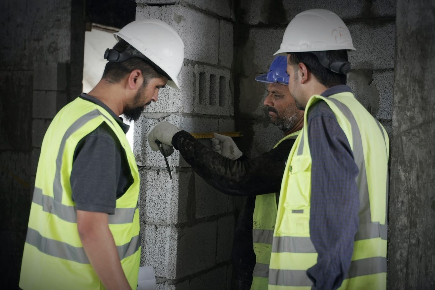 ثلاثة مهندسين بسترات السلامة يفحصون جداراً